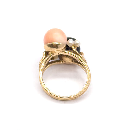 Upright rear view against white, looking through the open round shank to the yellow gold cup beneath the peachy pink orb, with two seed pearls and the dark coral orb behind.