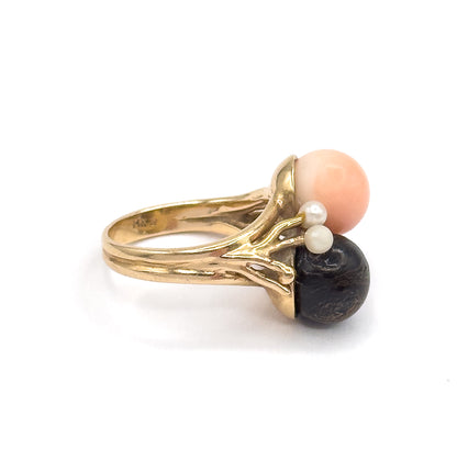 Profile view against white with the shank turned side-on, showing the stamp inside the band and the two seed pearls nestled where the peachy pink and dark coral orbs meet.