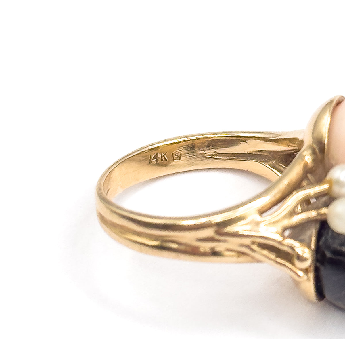 Close crop on the inside of the yellow gold band and its small stamp, with the split shank branching into openwork shoulders as the peachy pink and dark coral orbs sit at the frame's edge.