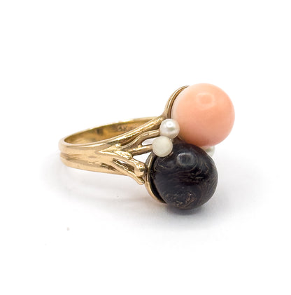 Angled side view against white showing the textured branch-like shoulders rising from the split shank to hold the peachy pink orb above and the dark coral orb below, with seed pearls between.