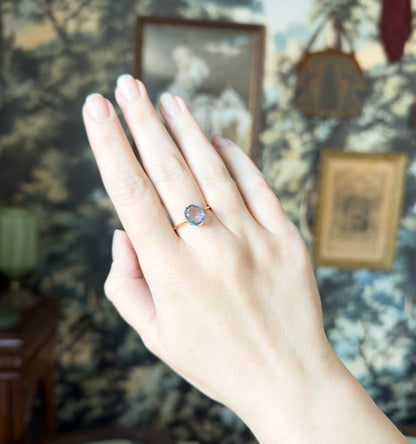 Full view of the hand raised against a leafy patterned backdrop, the small ring sitting low on the ring finger so its modest size against the whole hand is clear.