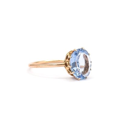 Profile view on a plain white background, the ring resting on its slim yellow gold shank with the oval glass stone raised in its pronged, scalloped gallery.