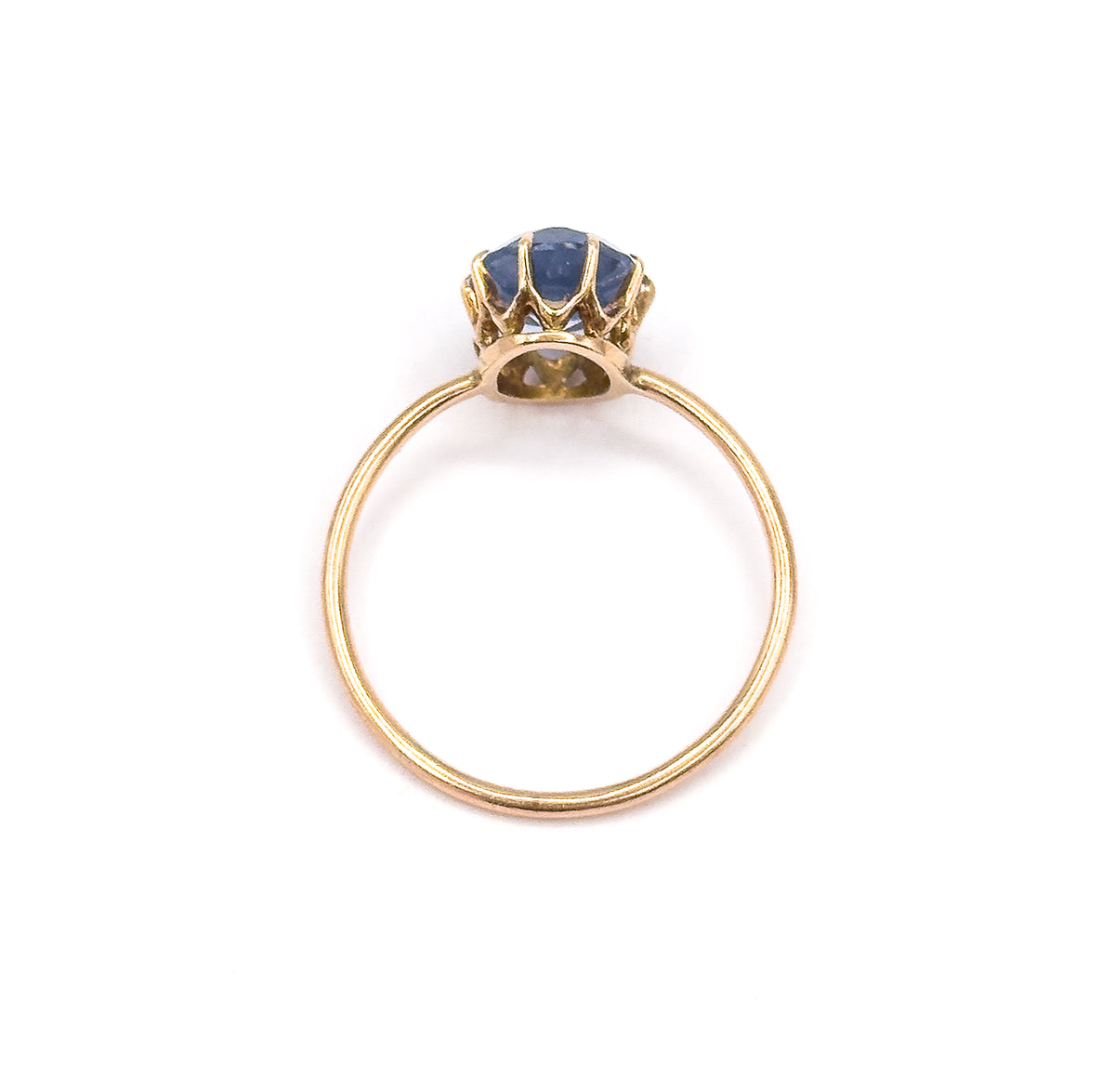 Viewed head-on through the circle of the shank, the ring stands upright so the open back of the gallery and the underside of the purplish blue glass stone are visible between the prongs.