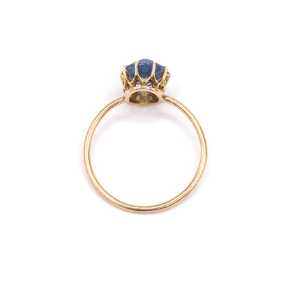 Viewed head-on through the circle of the shank, the ring stands upright so the open back of the gallery and the underside of the purplish blue glass stone are visible between the prongs.