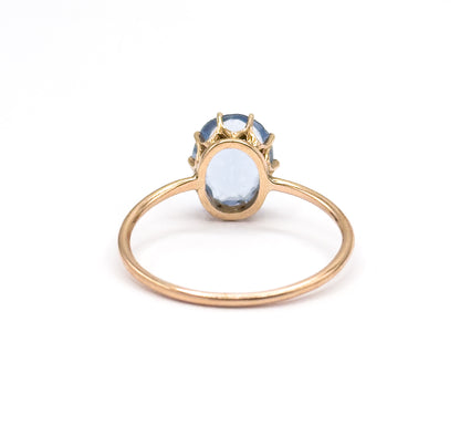 Almost the same view with slightly different angle, the upright ring seen from behind so the prong tips rise above the purplish blue glass stone and the thin round shank frames it.
