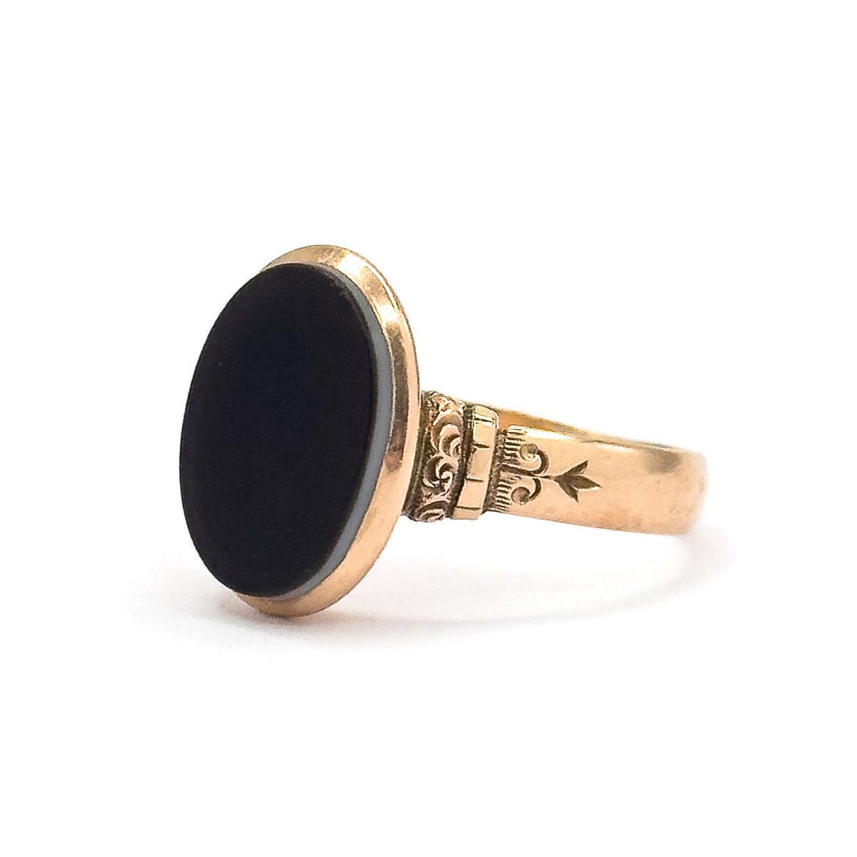 Profile facing left against white, the black oval agate presented nearly face-on with a pale stripe along its rim, and a ridged collar linking the deep bezel to the star-engraved shoulder.