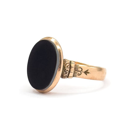 Profile facing left against white, the black oval agate presented nearly face-on with a pale stripe along its rim, and a ridged collar linking the deep bezel to the star-engraved shoulder.