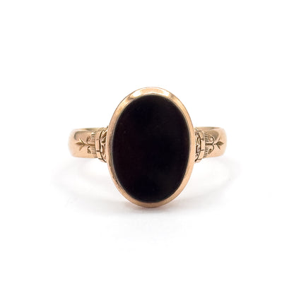 Closer crop of the face against white, the black agate oval filling its yellow gold bezel while the engraved leaf-and-scroll motifs on both shoulders read clearly beside the ridged collars.