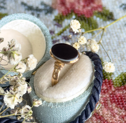 Propped in a pale blue velvet ring box among dried baby's-breath sprigs and a floral tapestry, the black-and-white banded agate and engraved shoulders angled up toward the camera.