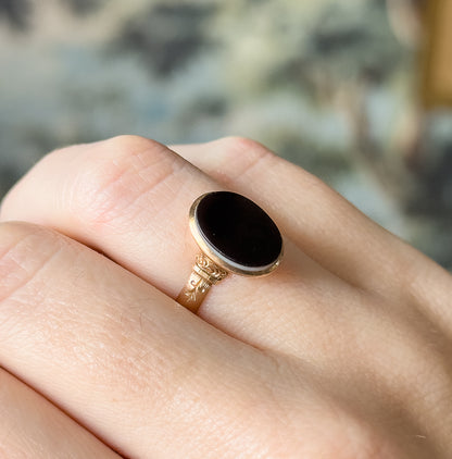 Shown on a finger from above and slightly ahead, the hand giving a sense of scale as the oval agate's white stripe shows along the lower bezel edge.