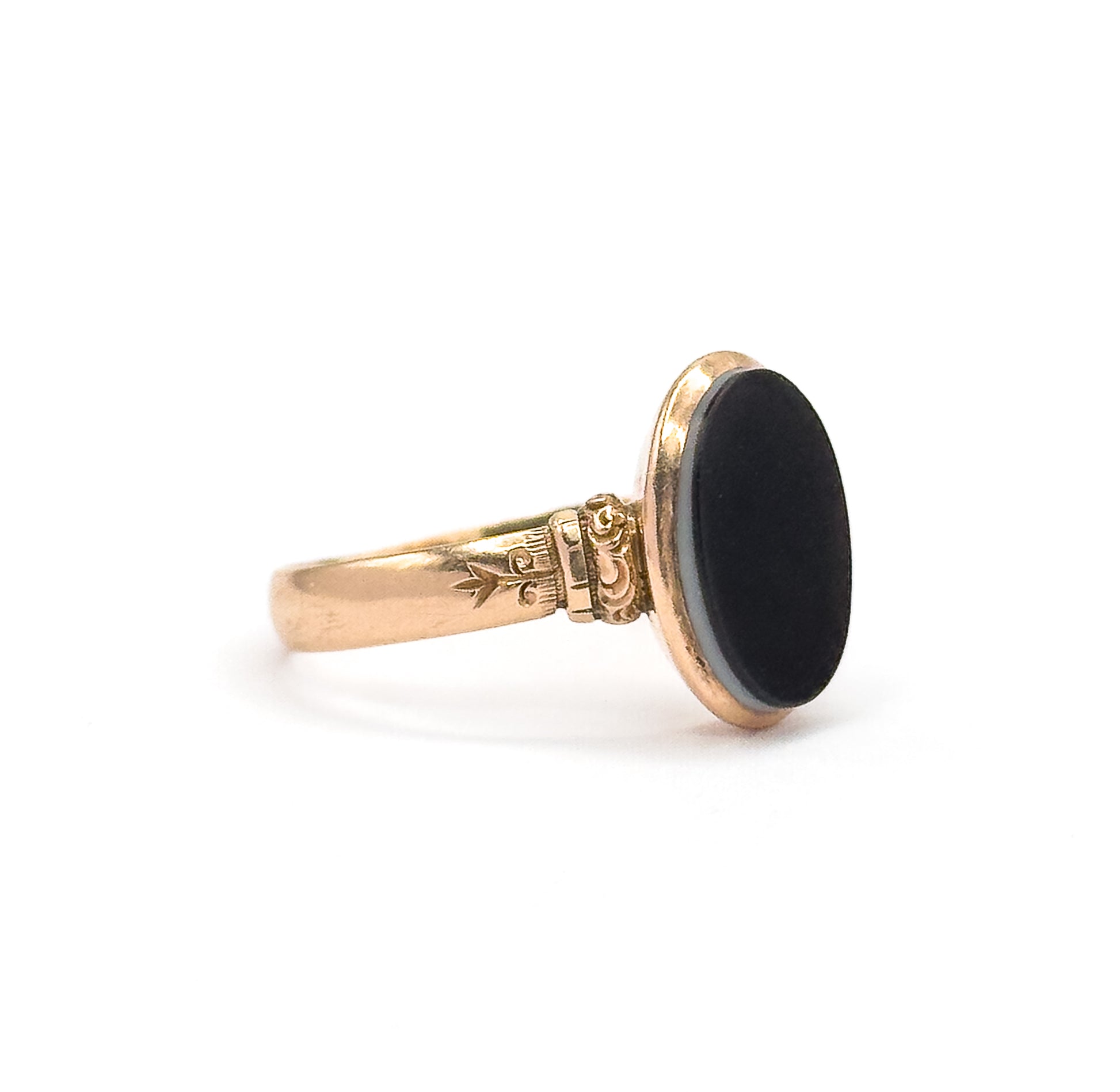 Seen from the side against white, the oval agate tilted nearly edge-on so its thickness and pale banding show at the bezel rim, with the engraved shoulder scrollwork in clear profile.