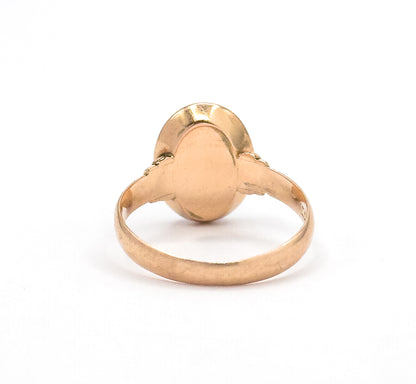 A closer rear view against white, filling the frame with the smooth closed back plate of the oval bezel and the flat rosy yellow shank curving away below it.