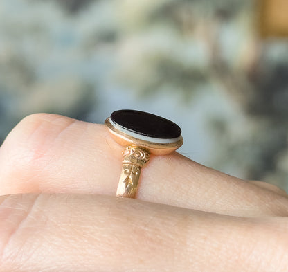 Victorian banded agate ring in 14K yellow gold, shown on a finger in close side view, the oval table-cut black stone with a white stripe raised in its smooth bezel above engraved shoulders.