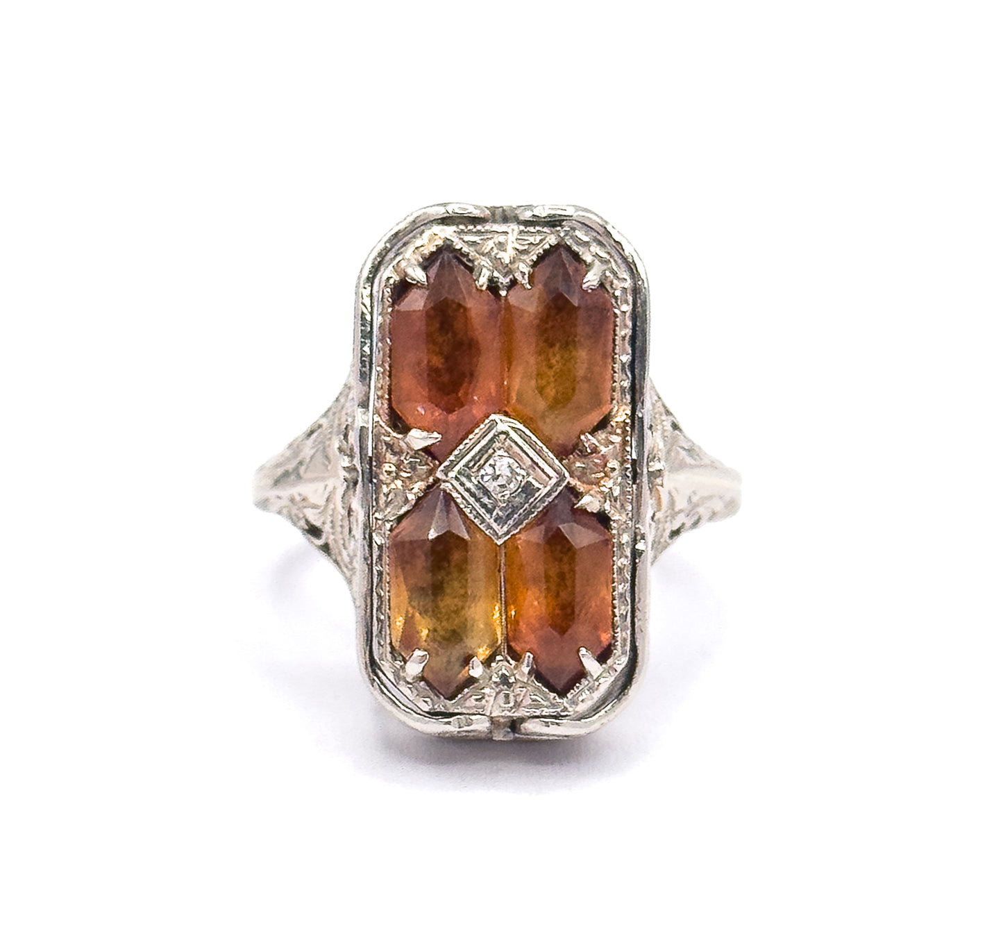 Close overhead view filling the frame with the rectangular face, showing each citrine's long faceted top, the corner prongs gripping them, and the diamond in its square bezel at the centre.