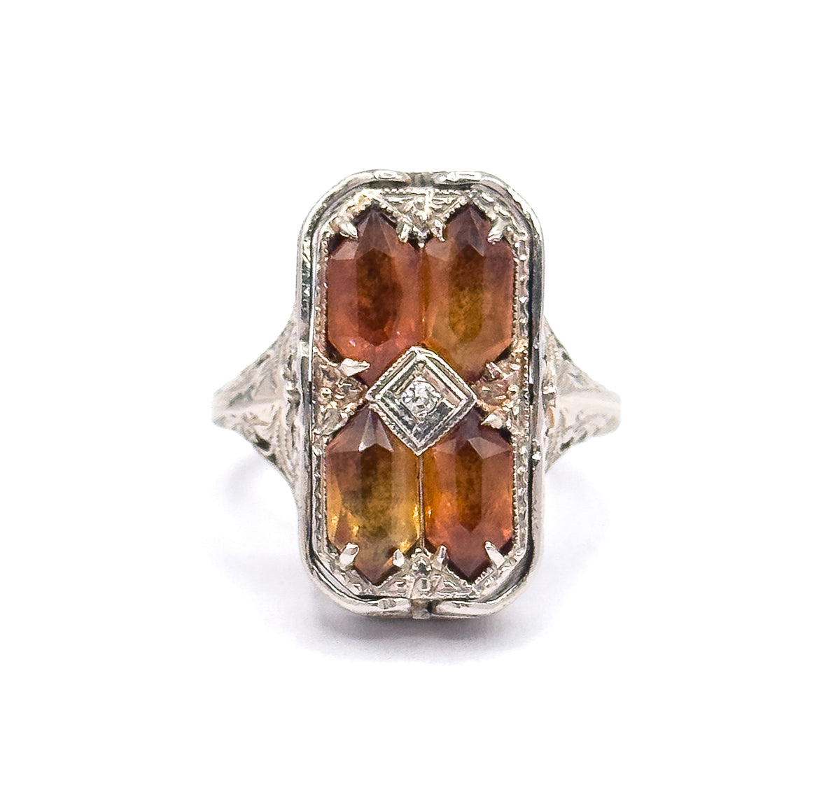 Close overhead view filling the frame with the rectangular face, showing each citrine's long faceted top, the corner prongs gripping them, and the diamond in its square bezel at the centre.