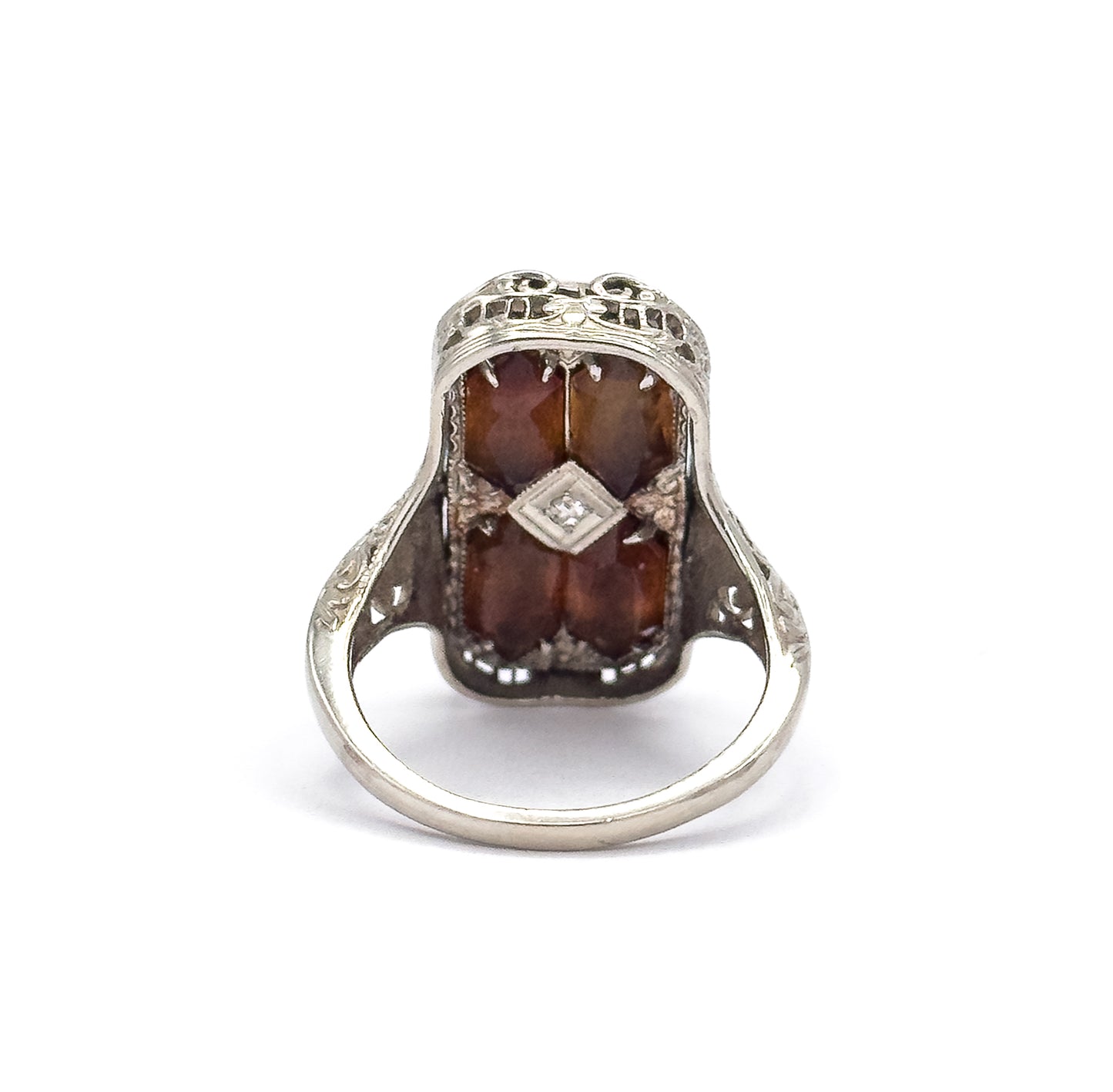 Upright view from the citrine side, looking through the open arch of the shank at the four prong-set orange stones and central diamond, with pierced filigree cresting above.