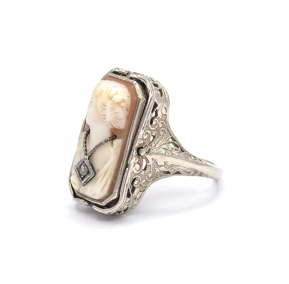 Steeply angled view from the cameo's lower corner, the tiny diamond-set necklace nearest the lens while the deep filigree side plate and its scroll piercing show the setting's height above the shank.