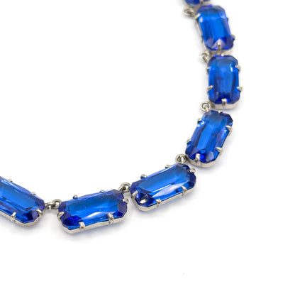 A diagonal run of the collar across white, with the small jump rings that join one pronged setting to the next clearly visible between the cobalt blue glass stones.