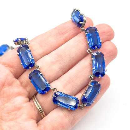 The necklace draped across an open palm, each cobalt blue glass stone about a finger-width wide in its pronged link, giving a clear sense of scale.