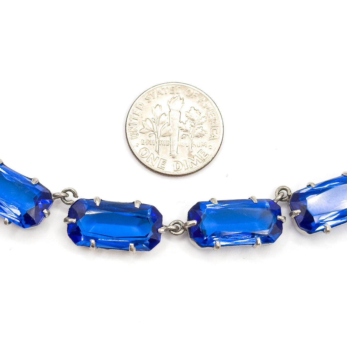 A dime rests above the row of links for scale, each cobalt blue glass stone roughly as long as the coin is wide within its pronged setting.