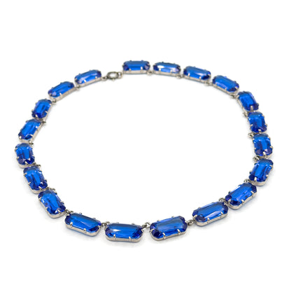 The whole collar laid flat in an open oval on white, clasp at the top and the largest cobalt blue glass links at the bottom front, showing how the row graduates around the neckline.
