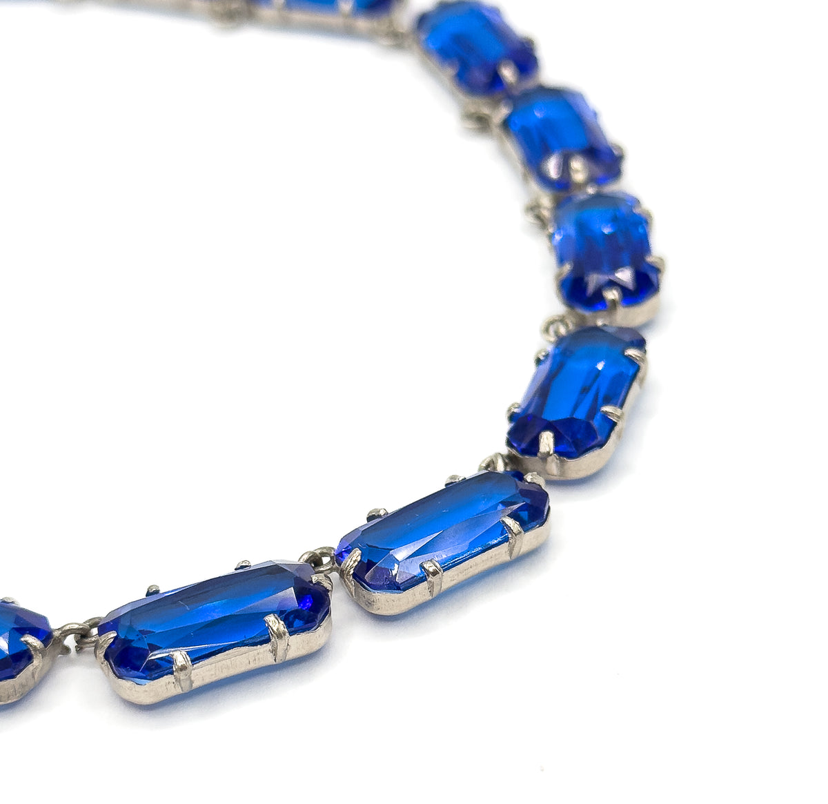 A steep close crop on the curve of the collar, where the light-coloured prongs grip each cobalt blue glass stone and the facets inside catch the light.