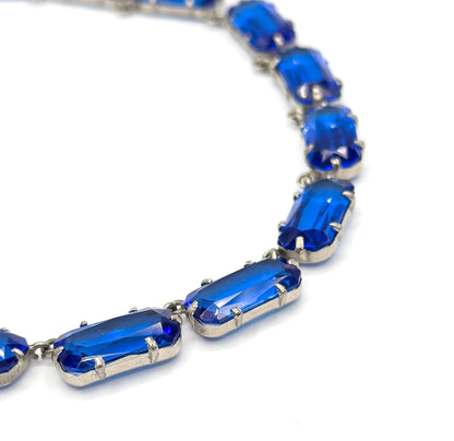 A steep close crop on the curve of the collar, where the light-coloured prongs grip each cobalt blue glass stone and the facets inside catch the light.