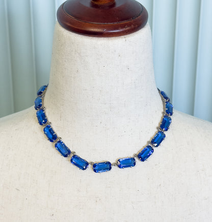 A collar necklace of cobalt blue glass stones in prong-set rectangular links, shown at the neck of a cream fabric display bust.