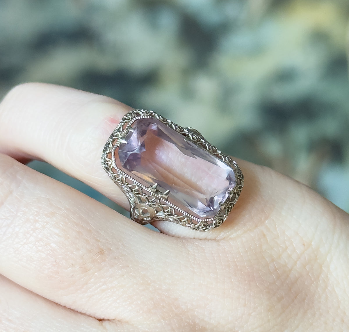Closer view shown on a finger from above, the pale purple stone's long facets catching light between double prongs, with the lace-like filigree gallery visible along the lower edge of the face.