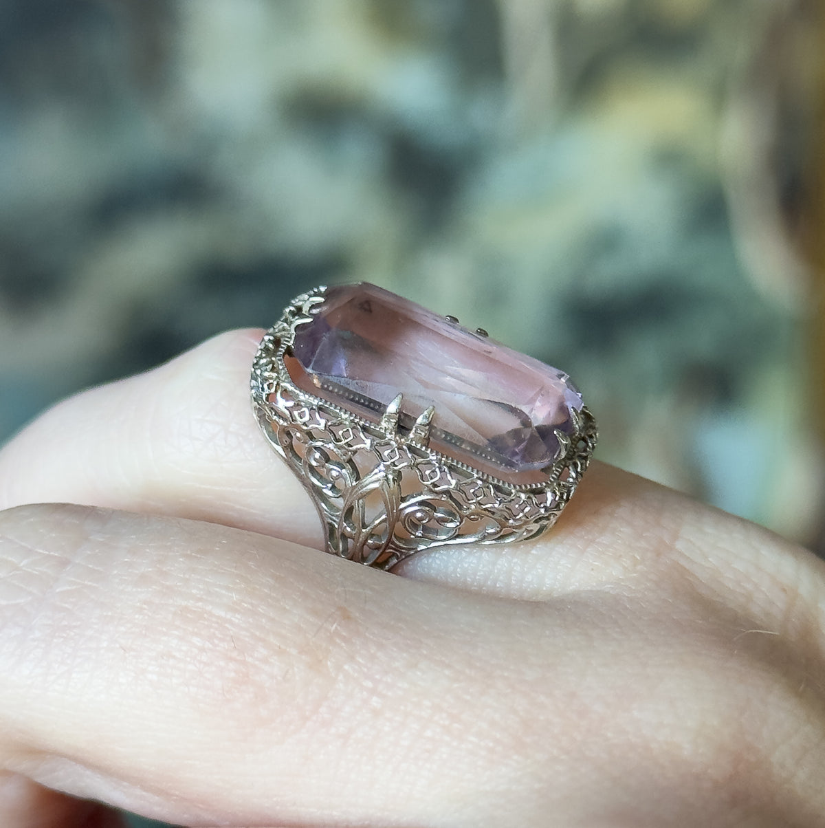 Low side-on view shown on a finger, revealing how high the head sits above the knuckle and the scrolled filigree gallery beneath the stone narrowing into the slender shank.