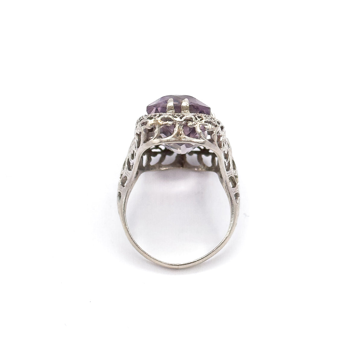 End-on view from the shank upward, the narrow band widening into the pierced filigree gallery with the double prongs and pale purple stone seen edge-on at the top.