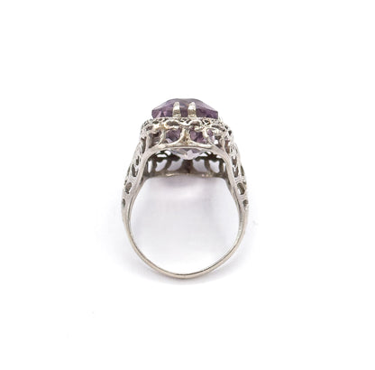 End-on view from the shank upward, the narrow band widening into the pierced filigree gallery with the double prongs and pale purple stone seen edge-on at the top.