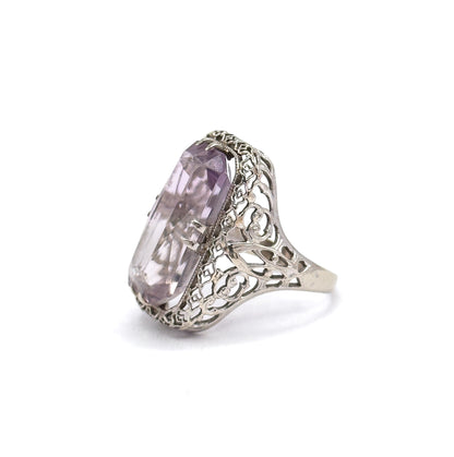 Angled from above the stone's long edge, light passes through the pale purple amethyst's facets while the scrolled filigree gallery and milgrain-edged sides recede toward the shank.