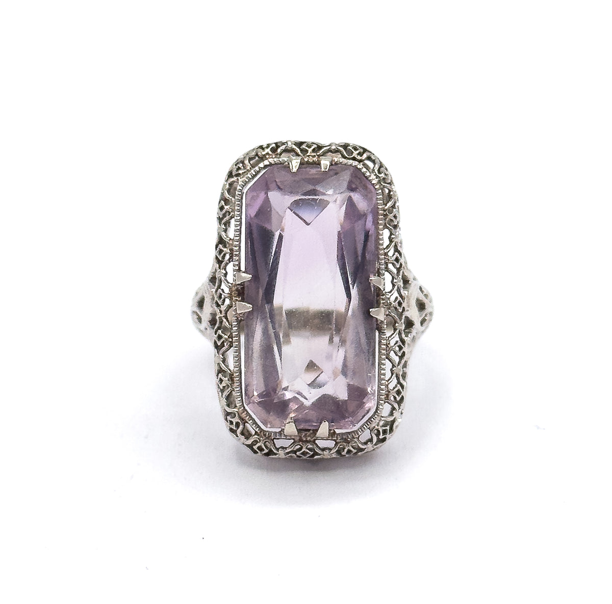Close face-on crop that brings the pierced scrollwork shoulders on either side of the head into view, flanking the pale purple stone in its double prongs.