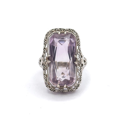Close face-on crop that brings the pierced scrollwork shoulders on either side of the head into view, flanking the pale purple stone in its double prongs.