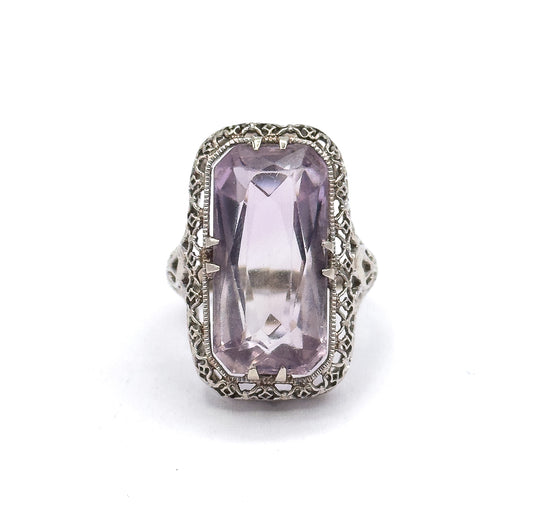 Close face-on crop that brings the pierced scrollwork shoulders on either side of the head into view, flanking the pale purple stone in its double prongs.