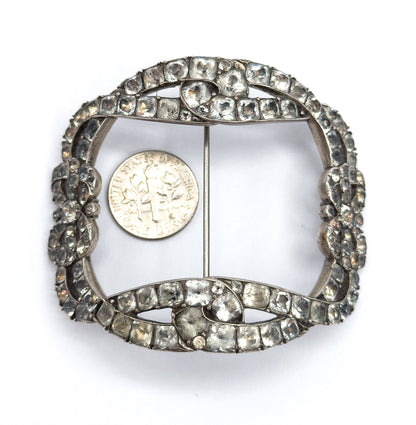 The whole buckle brooch flat with a dime resting inside its open centre for scale, the coin spanning little more than a third of the paste-set frame's width.