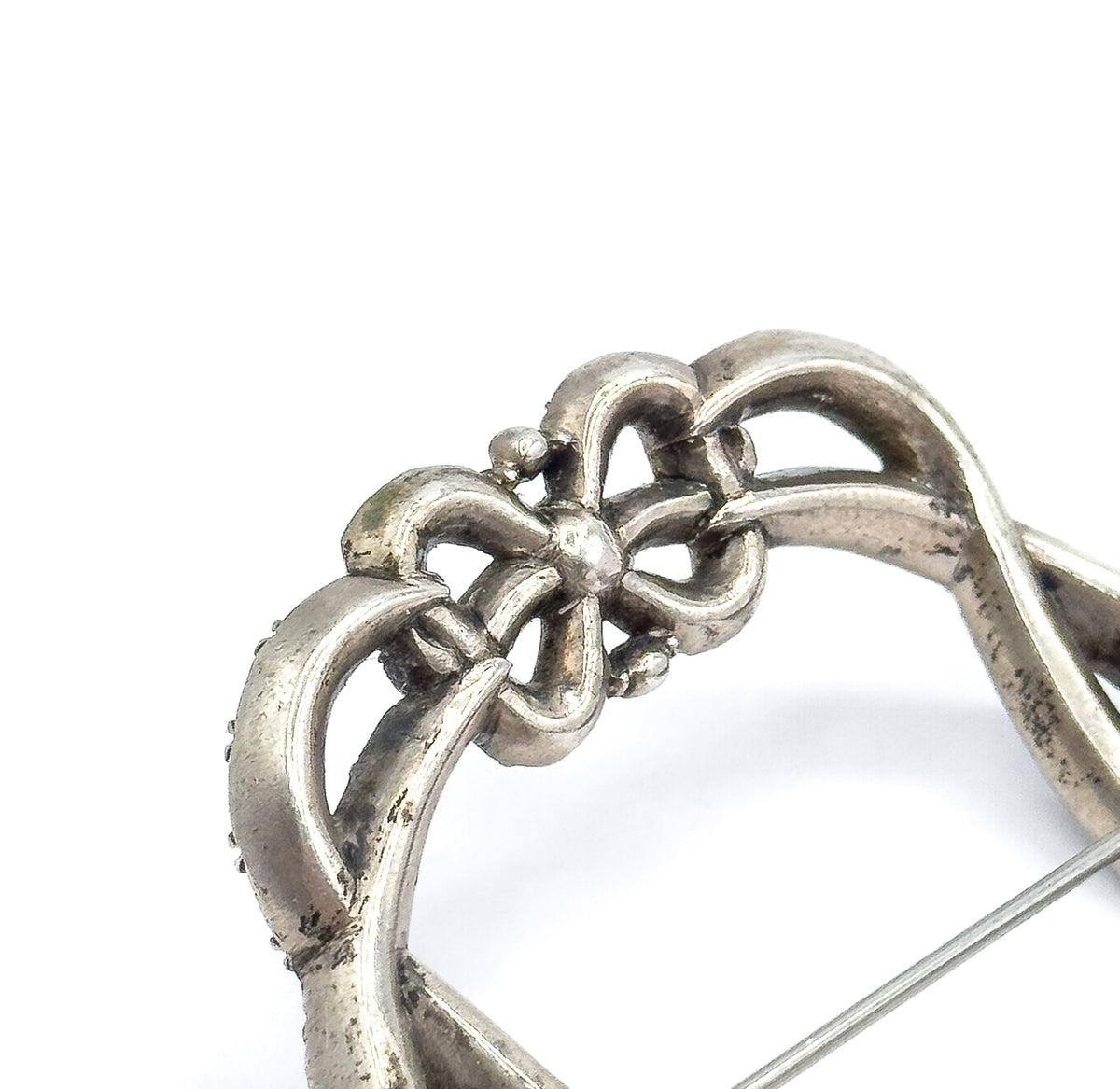 Close macro of the interlocking bow motif at the top of the frame, showing the sculpted sterling silver loops and small beaded accents, with the thin pin stem angling across at the lower right.