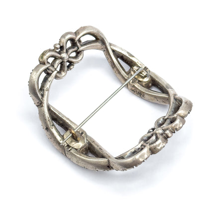 Angled reverse view on white, tilted to show the buckle's curved depth, with the pin stem running corner to corner between its small hinge fitting and the round catch.