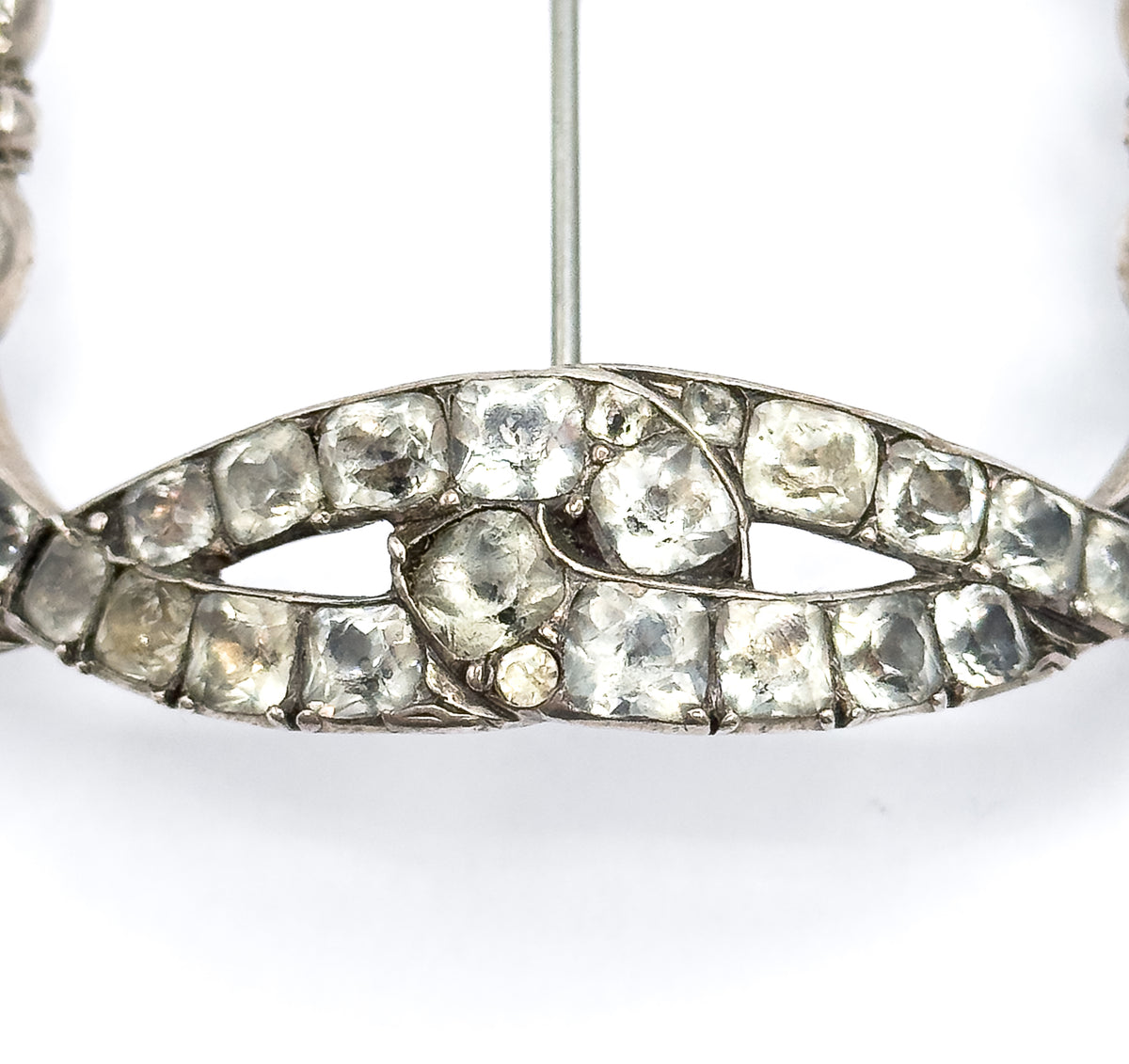Macro of the pointed lower bow crossing, its double rows of square hand-cut paste stones in silver collets meeting at a central stone, with the pin stem rising vertically behind.