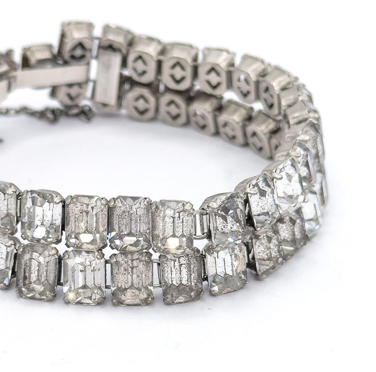Close-up of the curved band on a white background, showing the prong-set emerald cut glass stones in front and the open-backed settings along the reverse of the two rows behind.