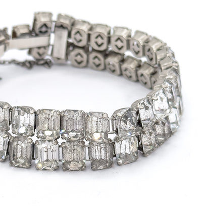 Close-up of the curved band on a white background, showing the prong-set emerald cut glass stones in front and the open-backed settings along the reverse of the two rows behind.