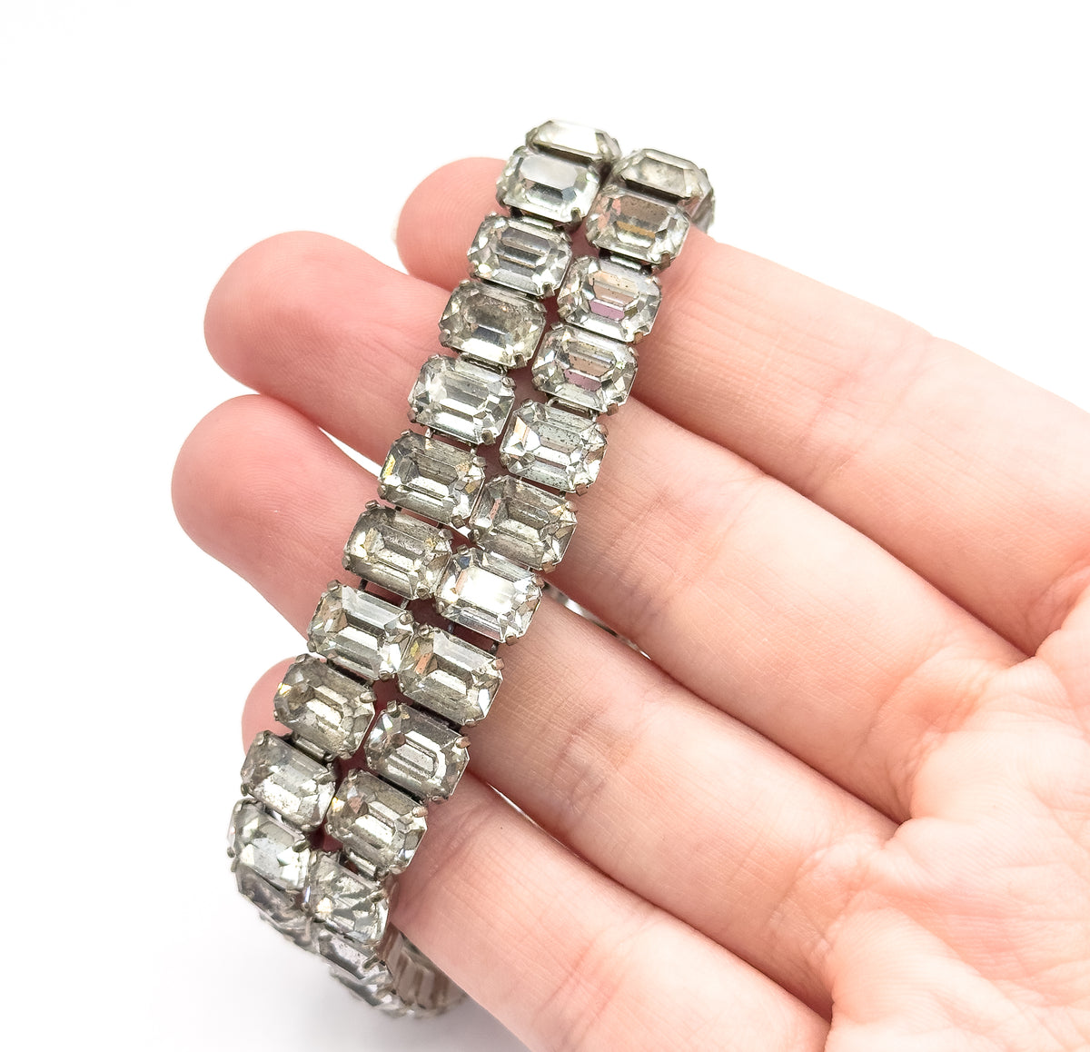 The bracelet laid across open fingers, giving a sense of scale as the two rows of emerald cut glass stones span roughly the width of four fingertips.