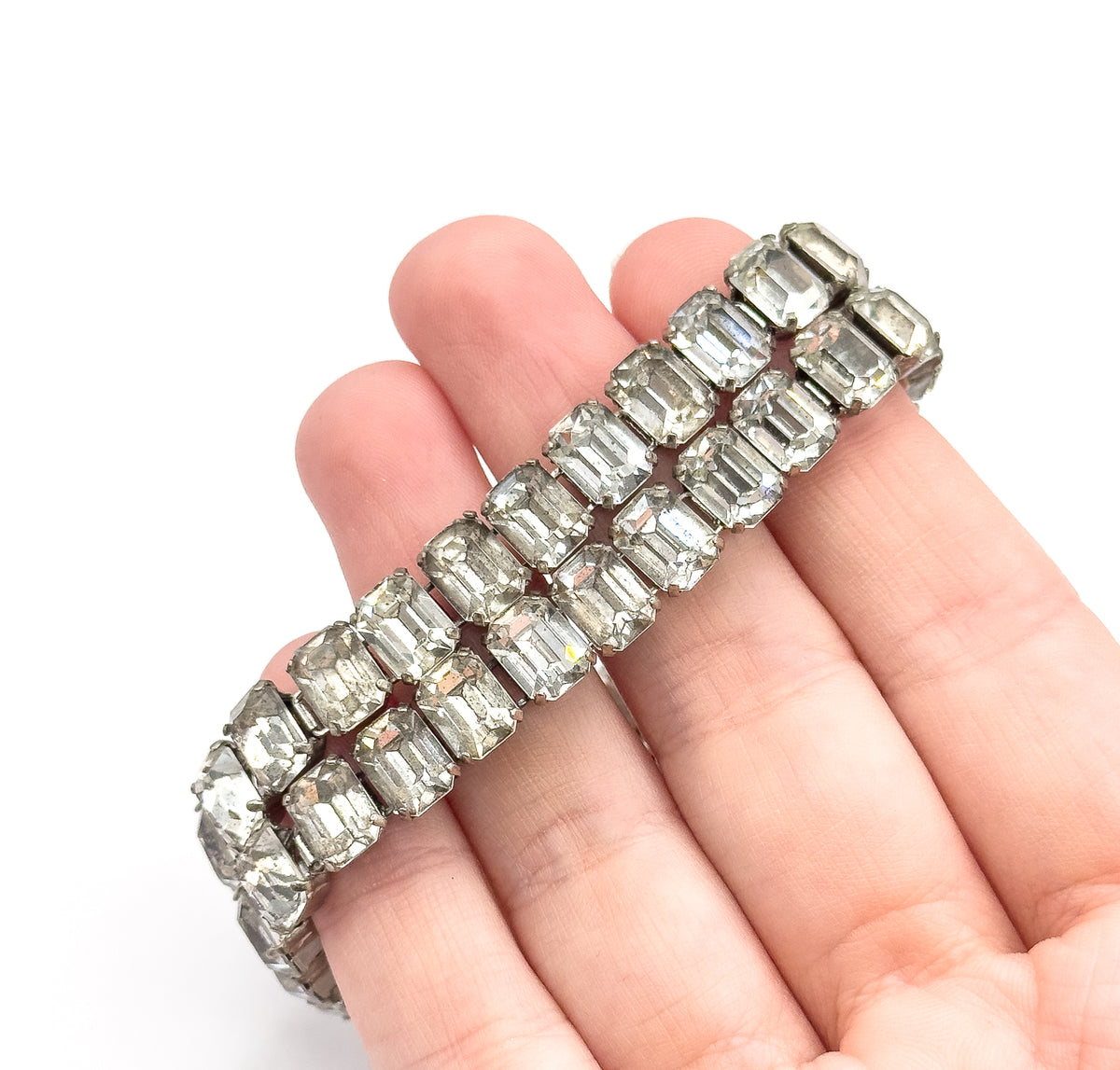 Closer angled view along the fingers, light catching each emerald cut stone so the tiny prongs and the narrow metal bars linking the two rows stand out against the skin.
