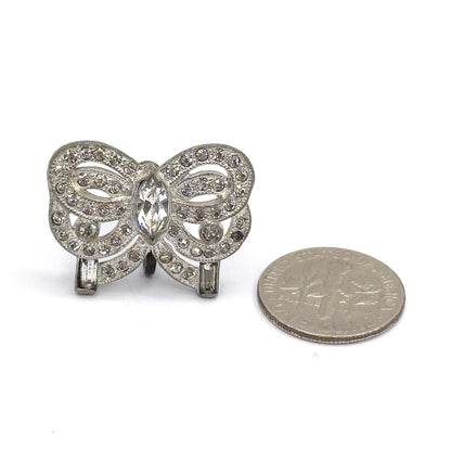 A single bow earring lies face-up beside a dime for scale, its marquise centre stone, round-stone loops and baguette ends filling a space about the width of the coin.