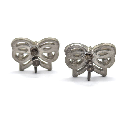 Both earrings stand upright side by side on their backs, showing the openwork bow frames from behind with each screw back's threaded post, knob and wire arm projecting toward the viewer.