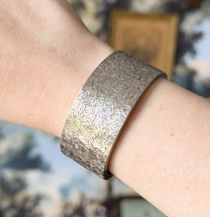 Close view of the cuff shown on the wrist, the hand-etched ivy pattern filling the wide band with darker patina settled into the recesses of the leaves.