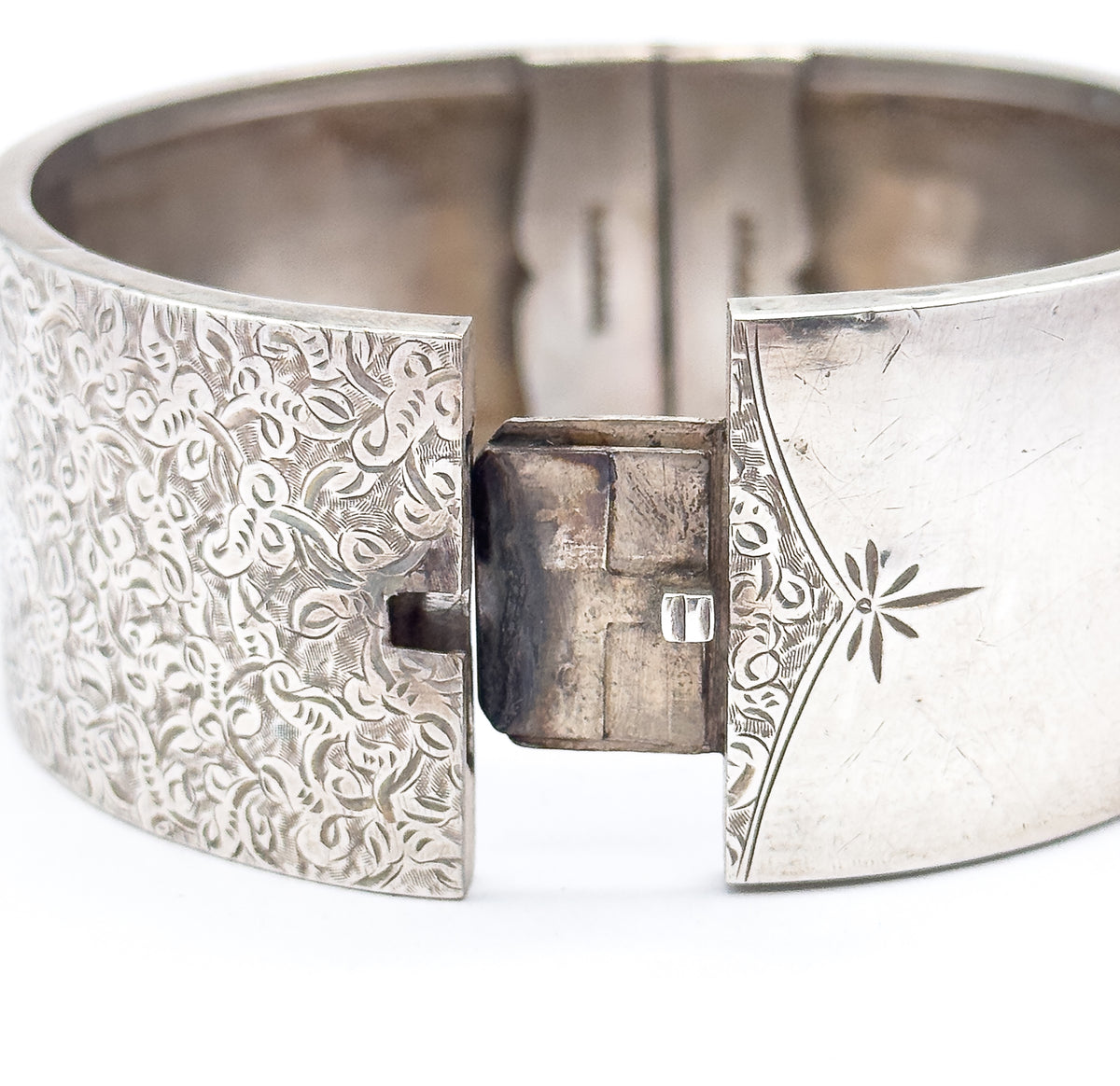The open box clasp seen close up, the projecting tongue standing between the ivy-etched end and the plain end with its engraved star and curved border line.