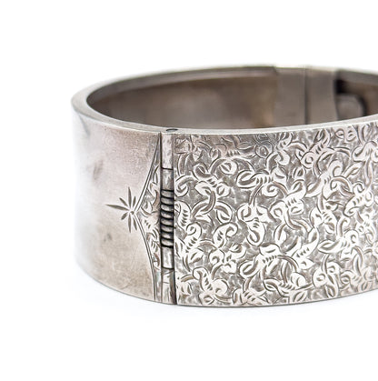 Angled close view of the hinge, where the plain end panel with its engraved star meets the ivy-etched band along a row of small knuckles.