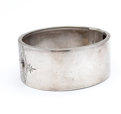 The closed cuff resting on its side against white, the plain end and its engraved star facing the camera while the ivy etching curves away at the left edge.